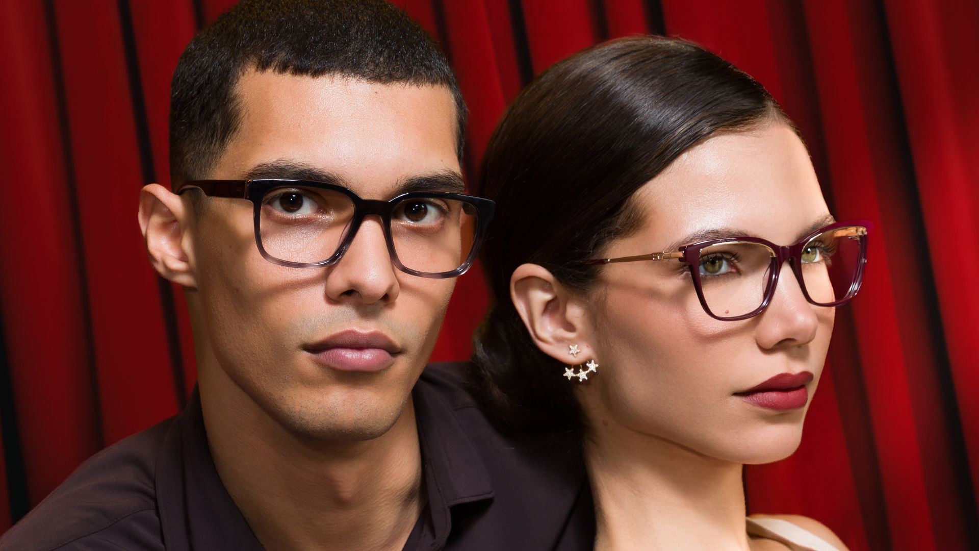 Couple wearing Biaggi optical frames in front of a red curtain